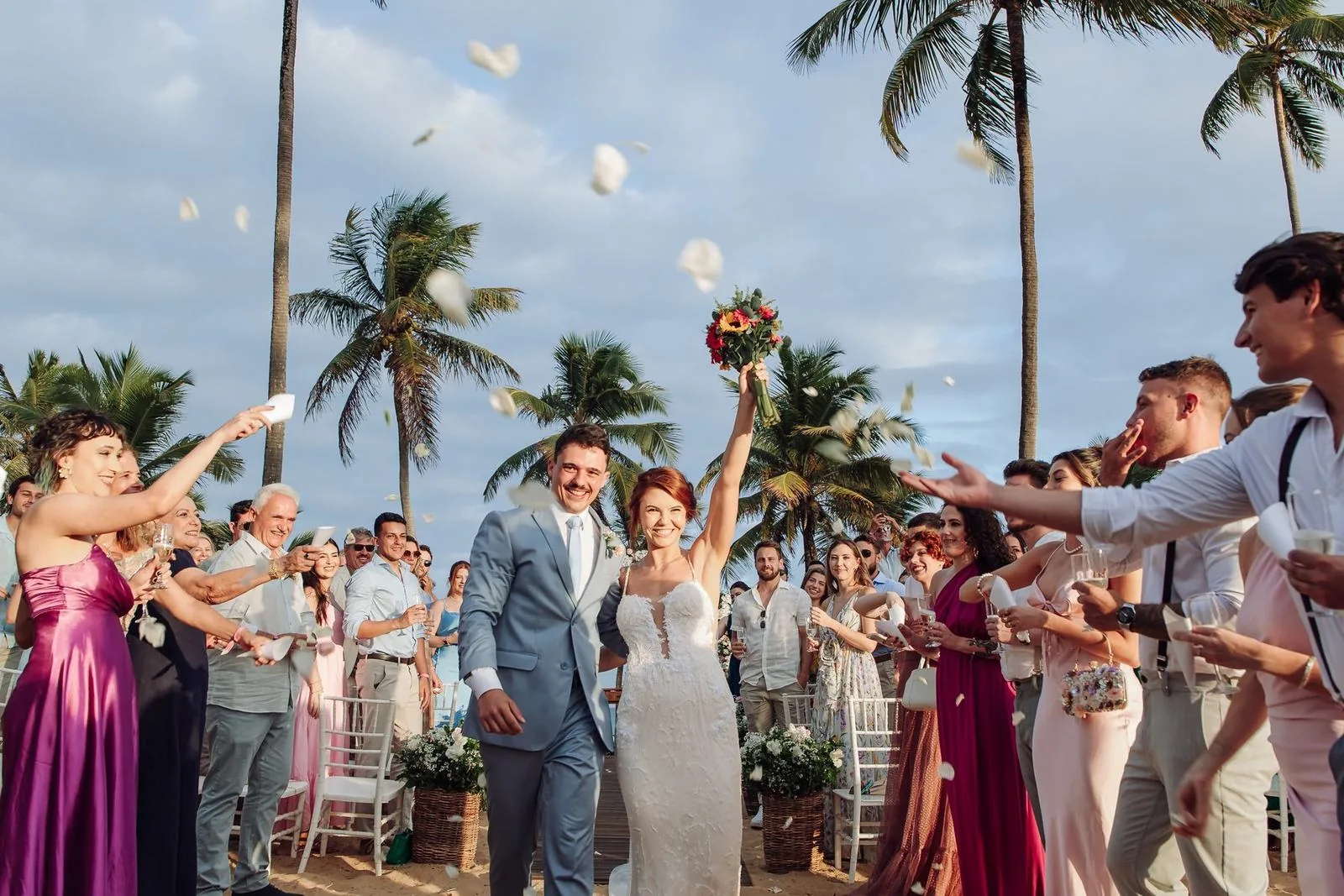 Casal sorrindo durante a cerimônia de casamento na praia, com os convidados em volta
