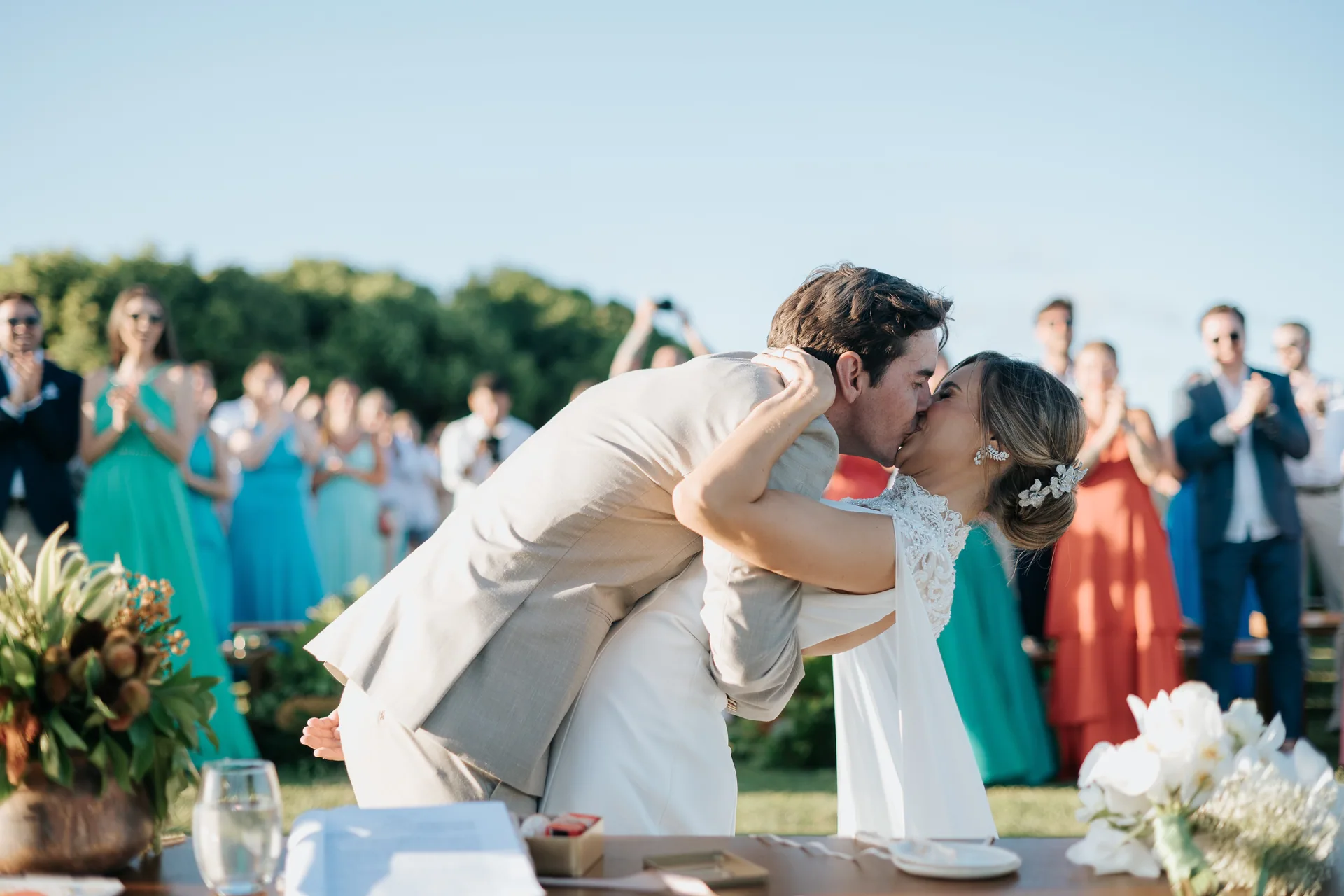 Casal se beijando na cerimônia, com os convidados aplaudindo ao fundo, no Nordeste