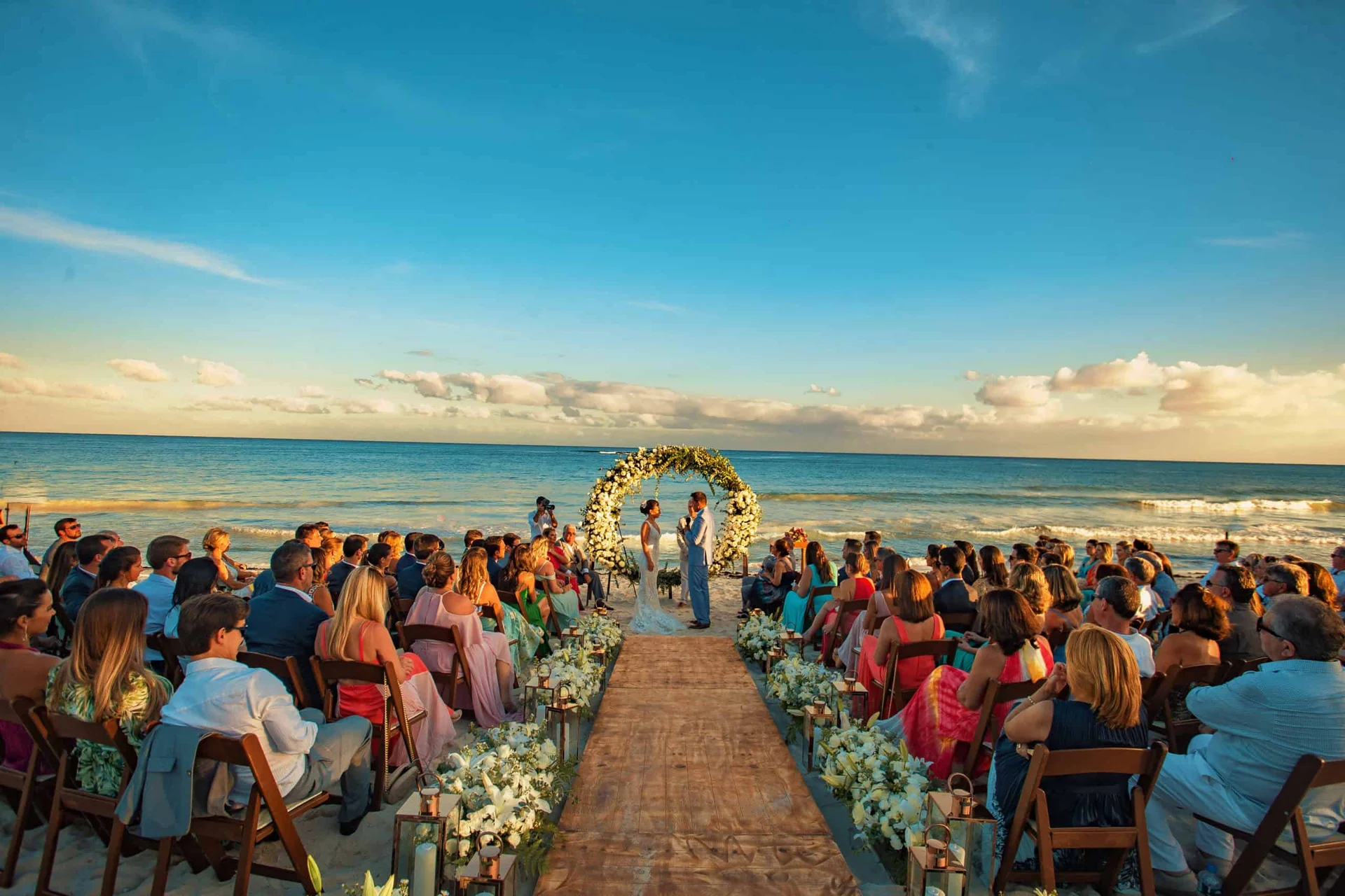 Cerimônia à beira-mar no fim da tarde, com o corredor de flores e os convidados sentados dos dois lados
