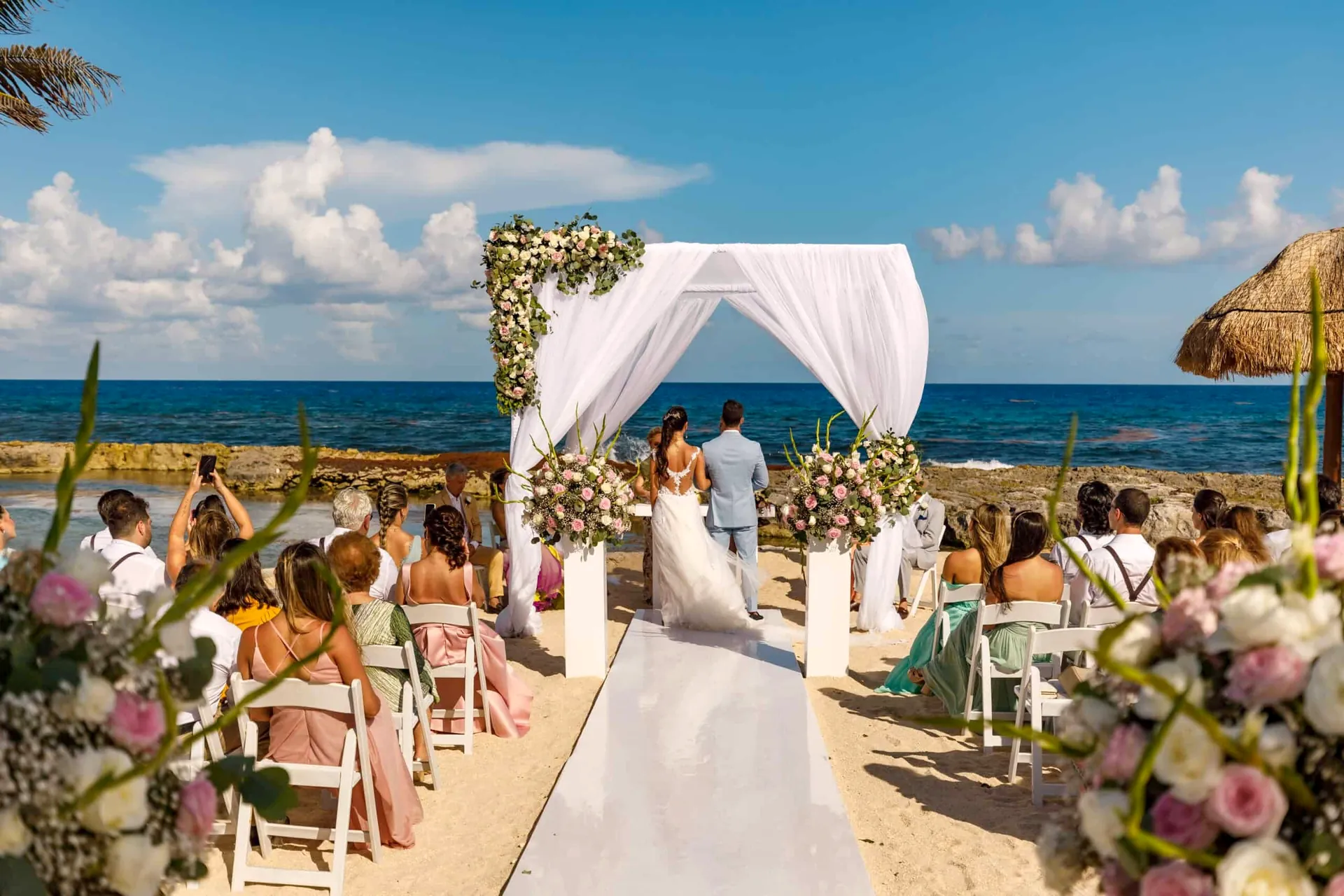 Cerimônia de casamento na praia da Riviera Maya, com o casal no altar sob o arco de flores e o mar do Caribe ao fundo