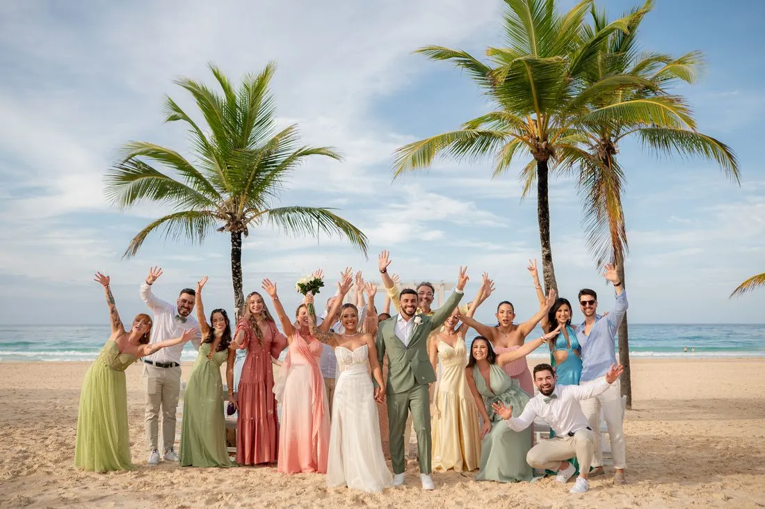 Casal com os convidados celebrando na praia, entre coqueiros
