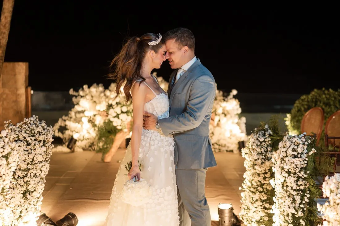 Victoria e Marco na cerimônia à noite, entre arranjos de flores