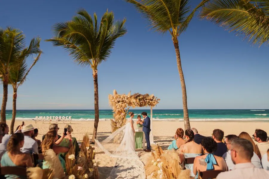 Cerimônia na praia de Punta Cana, com o casal no altar de flores entre coqueiros e o mar azul